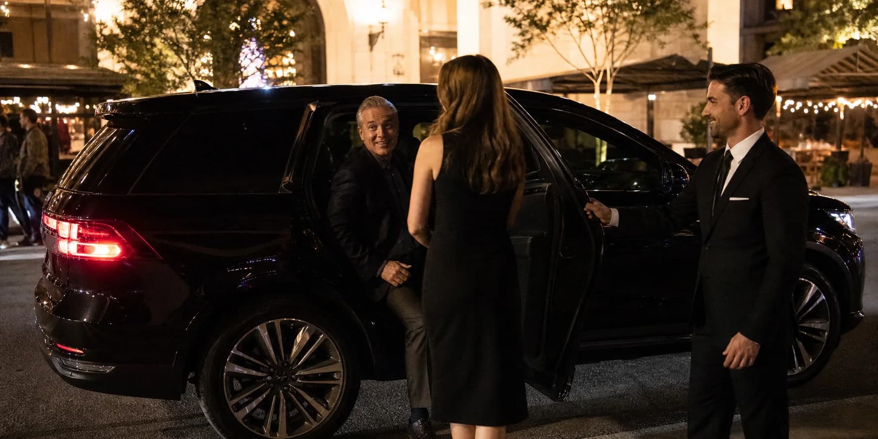 Chauffeur opening a black luxury vehicle for an evening point-to-point ride.